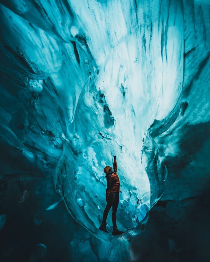 Woman reaching up in blue ice cave