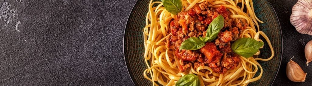 Bowl of pasta with tomato sauce and basil on dark grey background