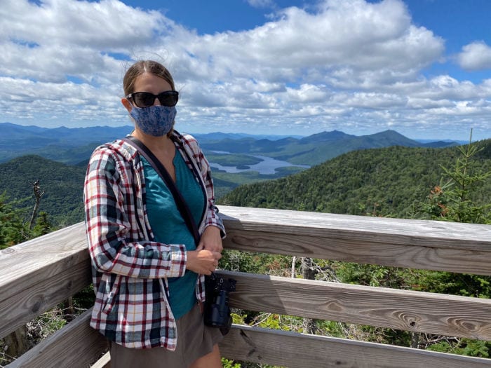 woman wearing face mask with view of Lake Placid in background from top of Little Whiteface Mountain