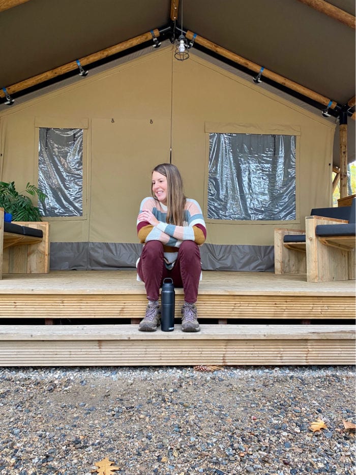 Woman in striped sweater sitting on porch steps of glamping tent