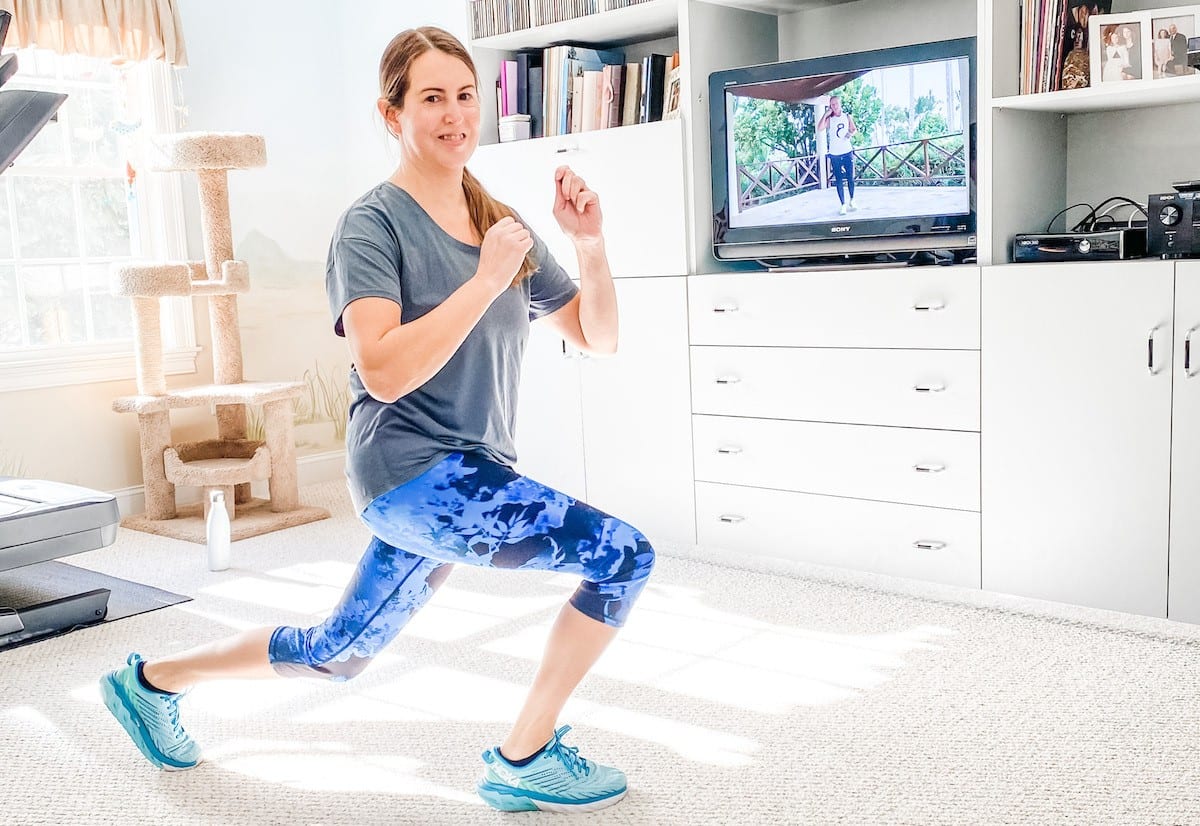 Woman exercising at home with tv in background showing exercise class