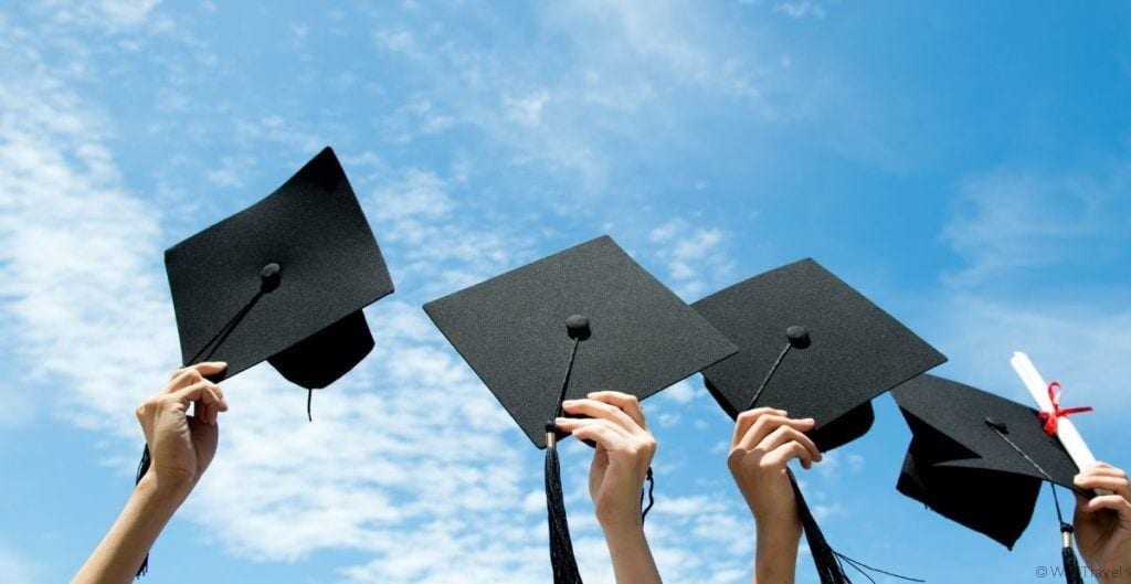 Graduation hats held in the air against a blue sky