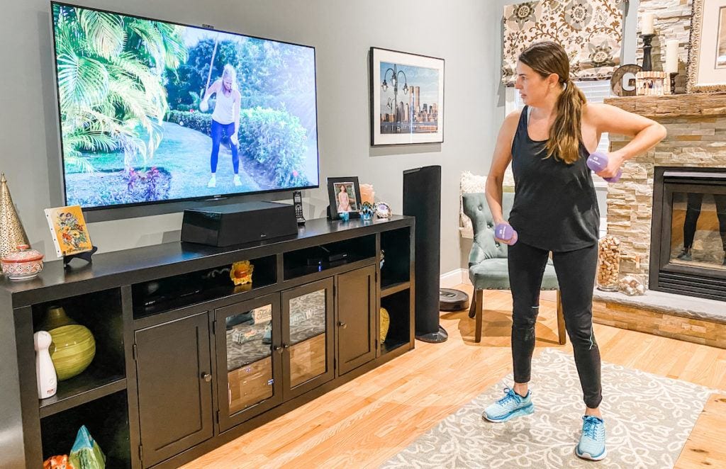 woman working out with hand weights in front of tv exercise class in family room