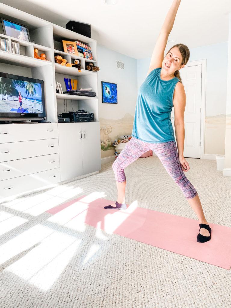 Woman doing standing yoga pose in front of tv with exercise class