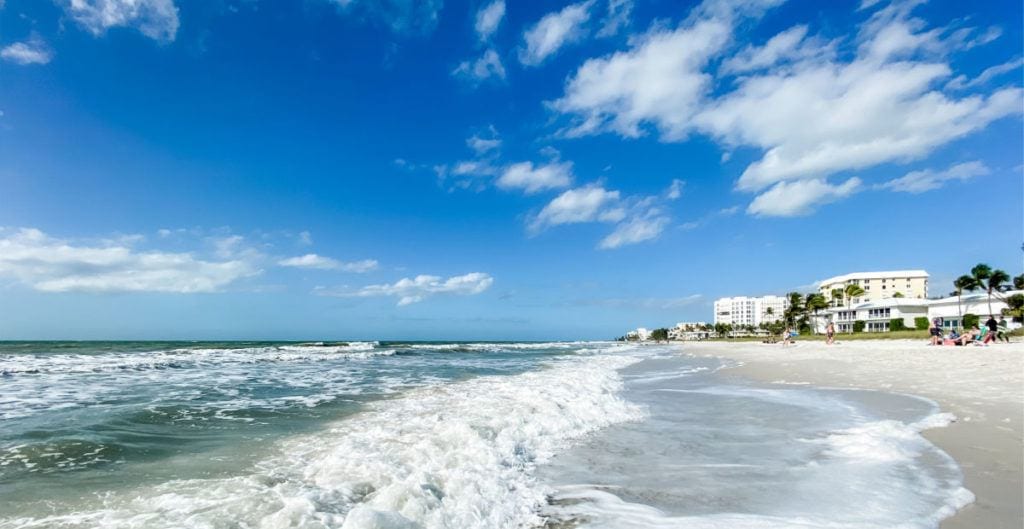 Lowdermilk beach waves crashing on the sand with hotels in the background and bright blue sky