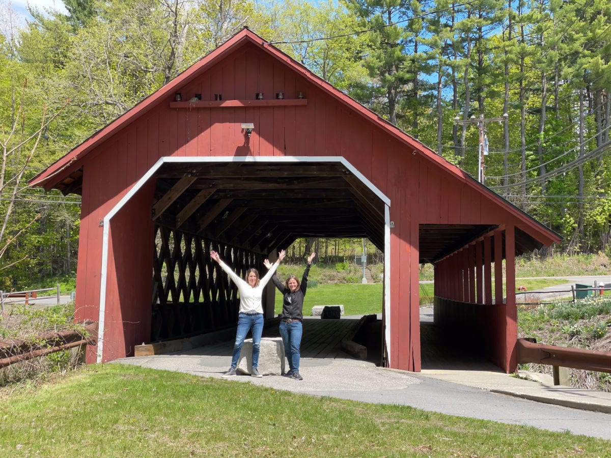 two women with their arms up standing at the entrance to a red covered bridge