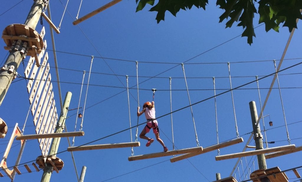 girl climbing on logs on tree top adventure course