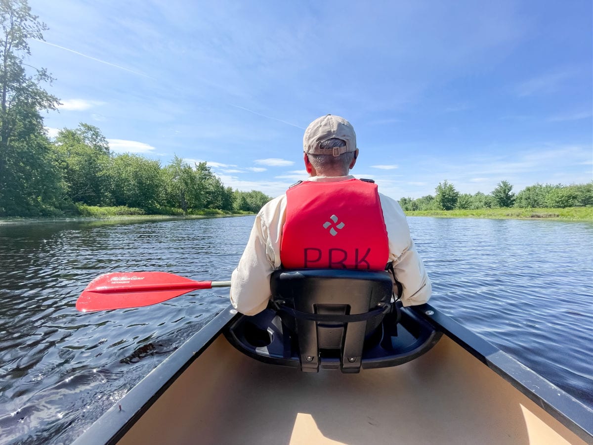Man in a red life jacket paddling canoe through Hirundo Wildlife Refuge