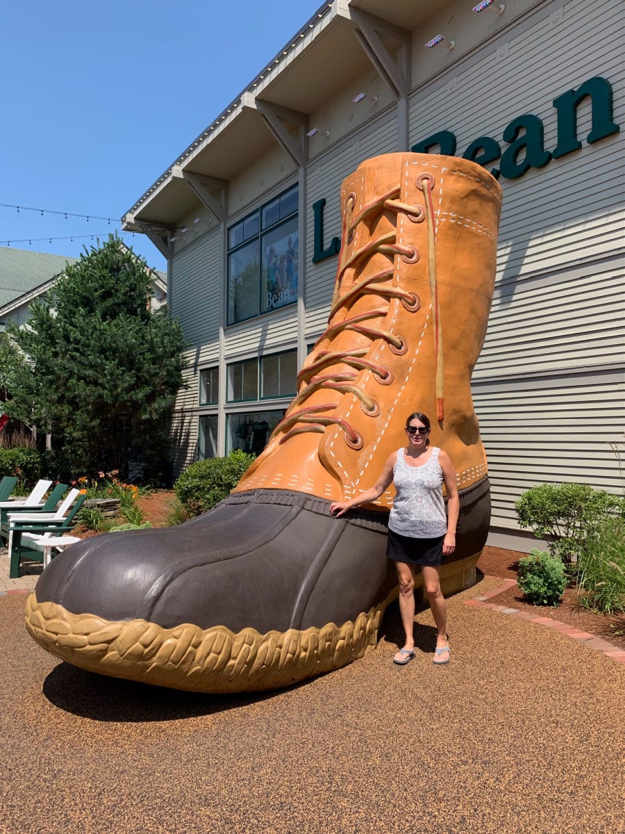 Woman standing in front of giant Bean Boot in front of the L. L. Bean company store in Freeport Maine