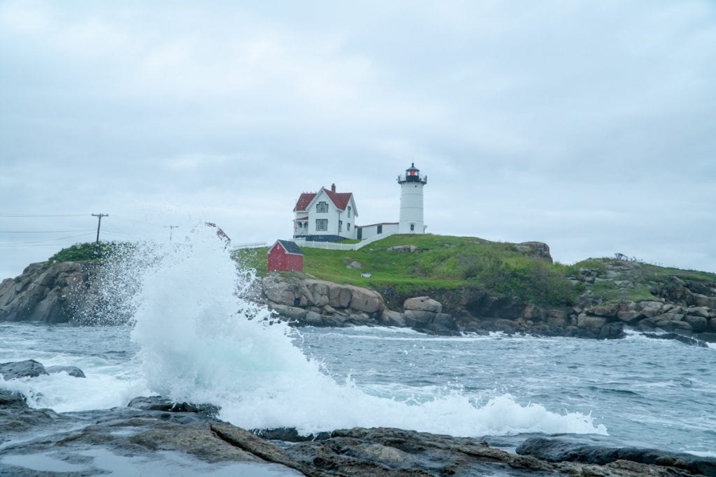 Nubble Lighthouse in Cape Neddick with a large wave splashing on the rocks in front