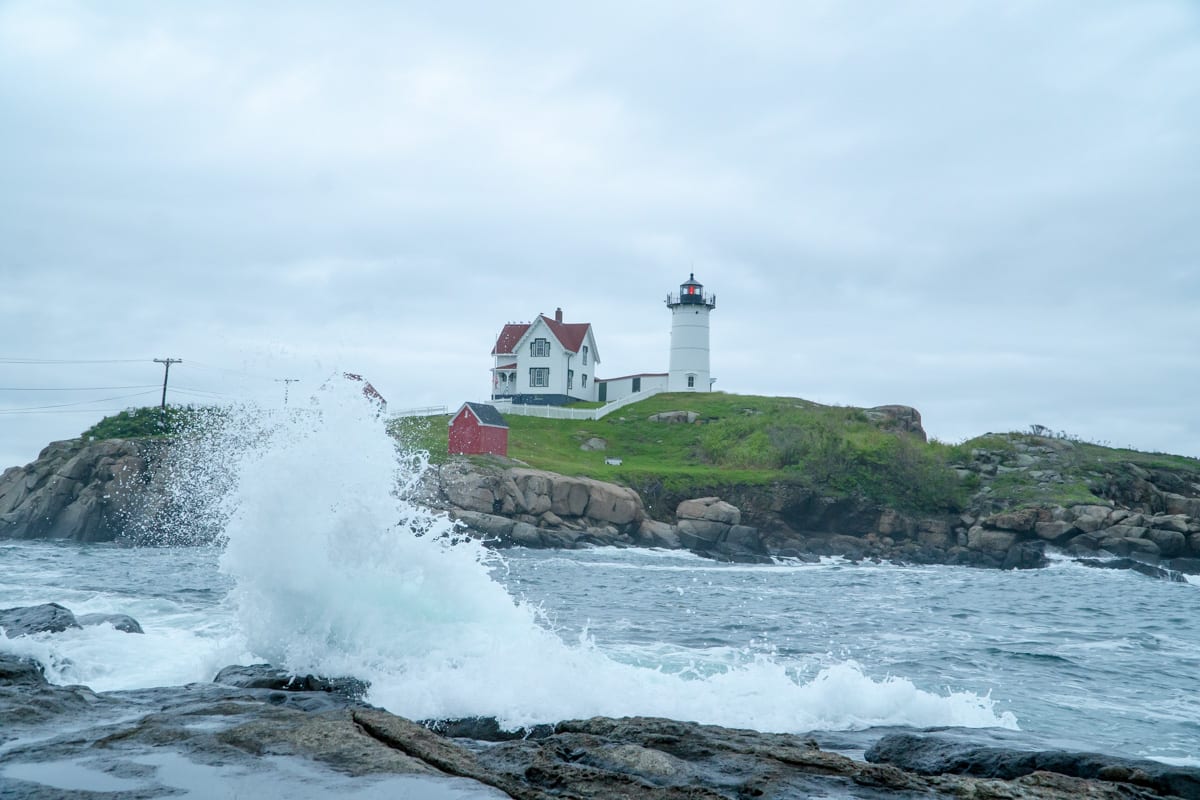 Nubble Lighthouse in Cape Neddick with a large wave splashing on the rocks in front