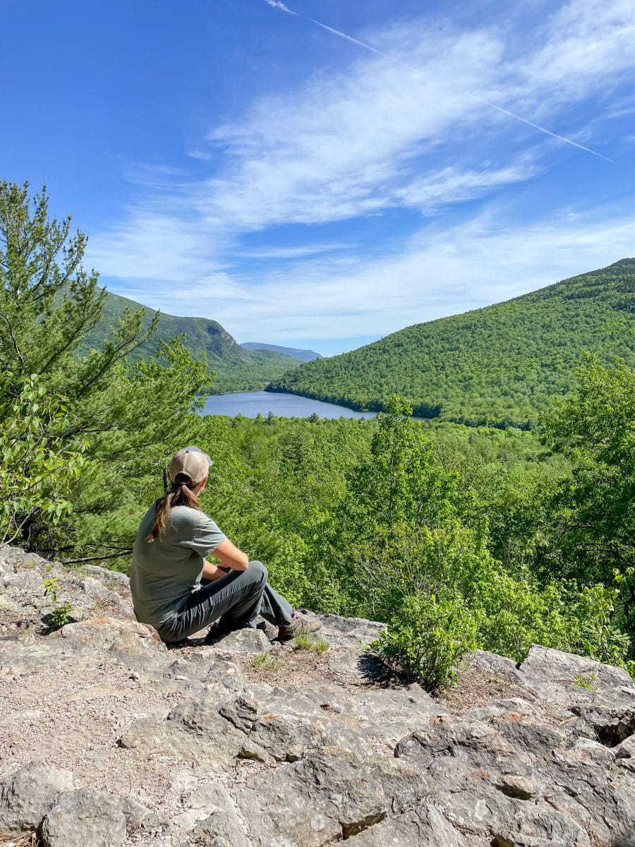 woman sitting on rock overlooking pond and valley