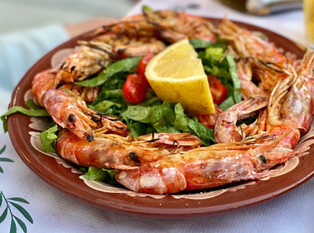 Large prawns on a brown plate with a lemon wedge and salad