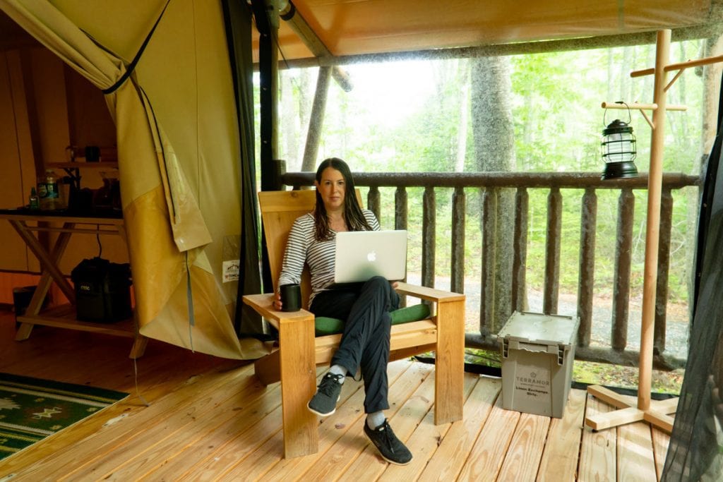 Woman sitting on porch of Bayberry tent with computer