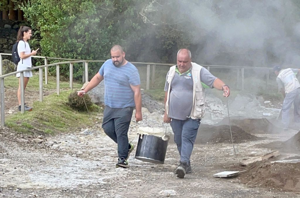 Two men carrying a pot of Cozido in Furnas