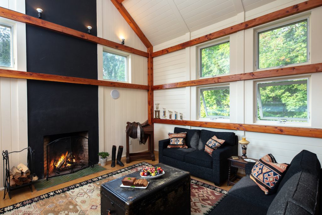 Winvian Farm stable room with white walls, wood beamed ceilings, black couches and a fireplace.