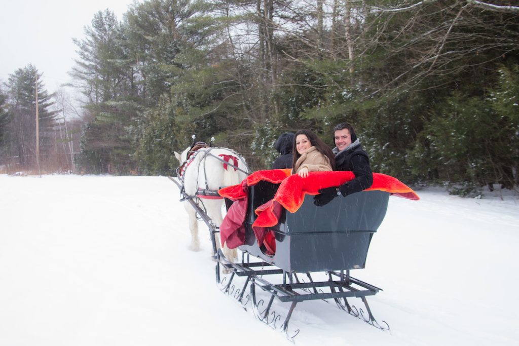 Couple in a horse drawn sleigh with a red blanket