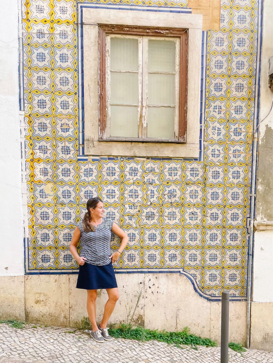 Woman standing in front of yellow and blue tiled building and window