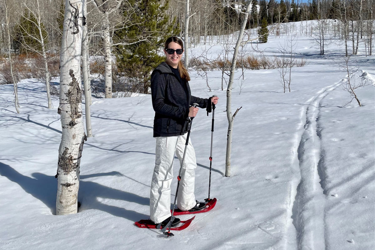 Woman in black coat and white snow pants snowshoeing 