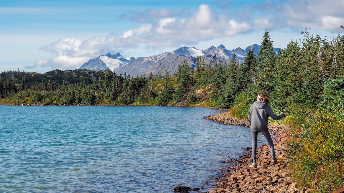 girl Skipping stones in lake with mountains in the background