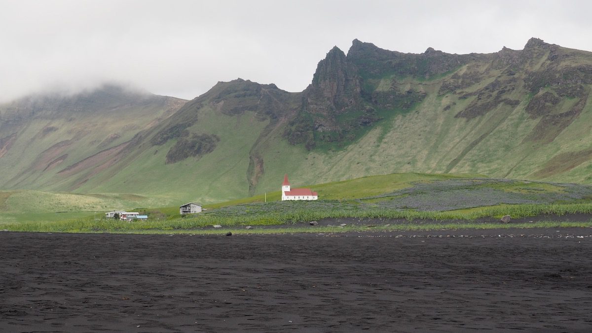 White church with red roof on a background against the green cliffs in Vik Iceland