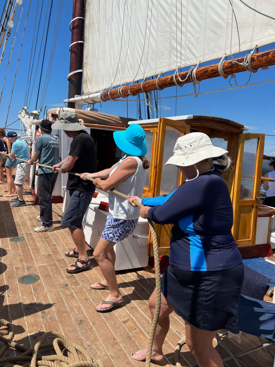 Passengers pulling on rope to raise the sails