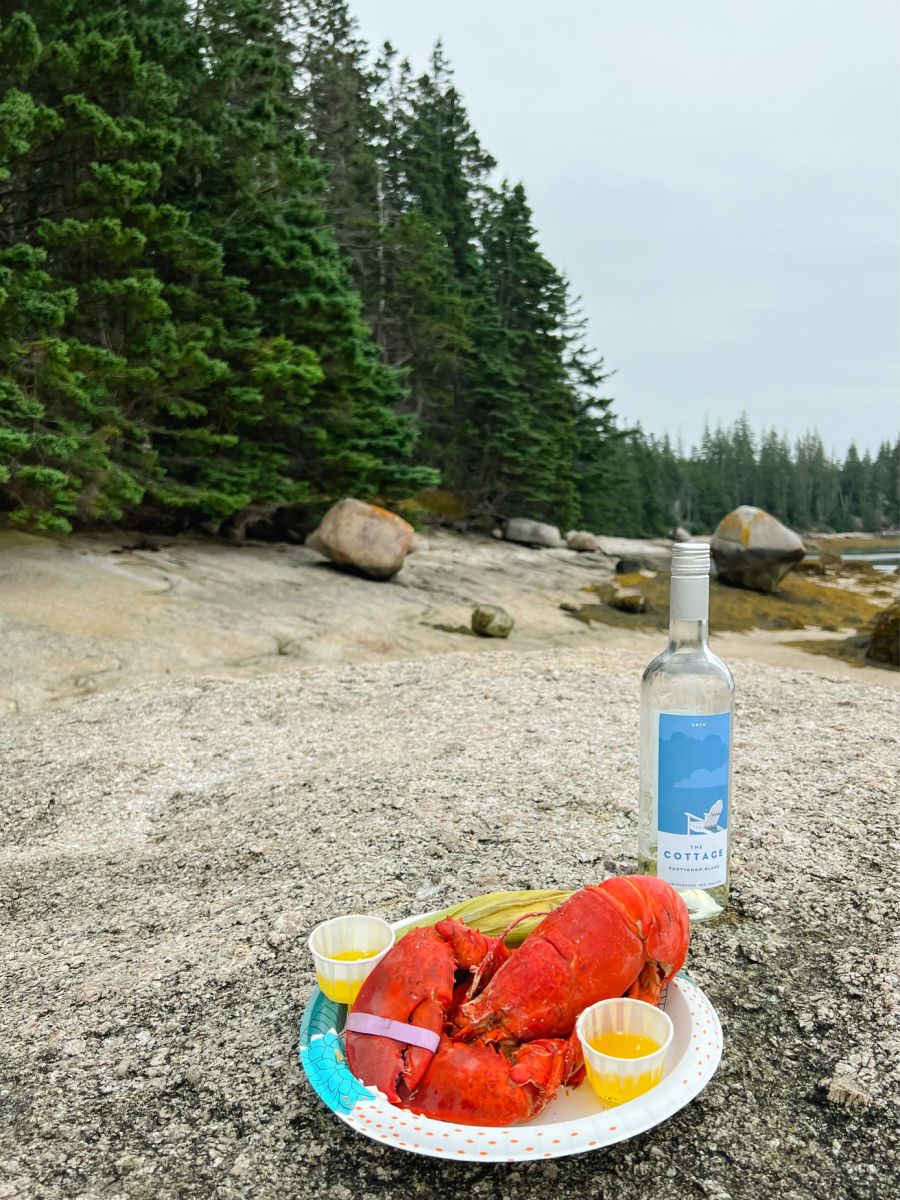 Lobster and corn on a plate sitting on a rock with a bottle of wine