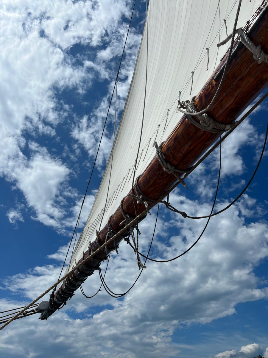Looking up at a white sail against the blue sky and clouds