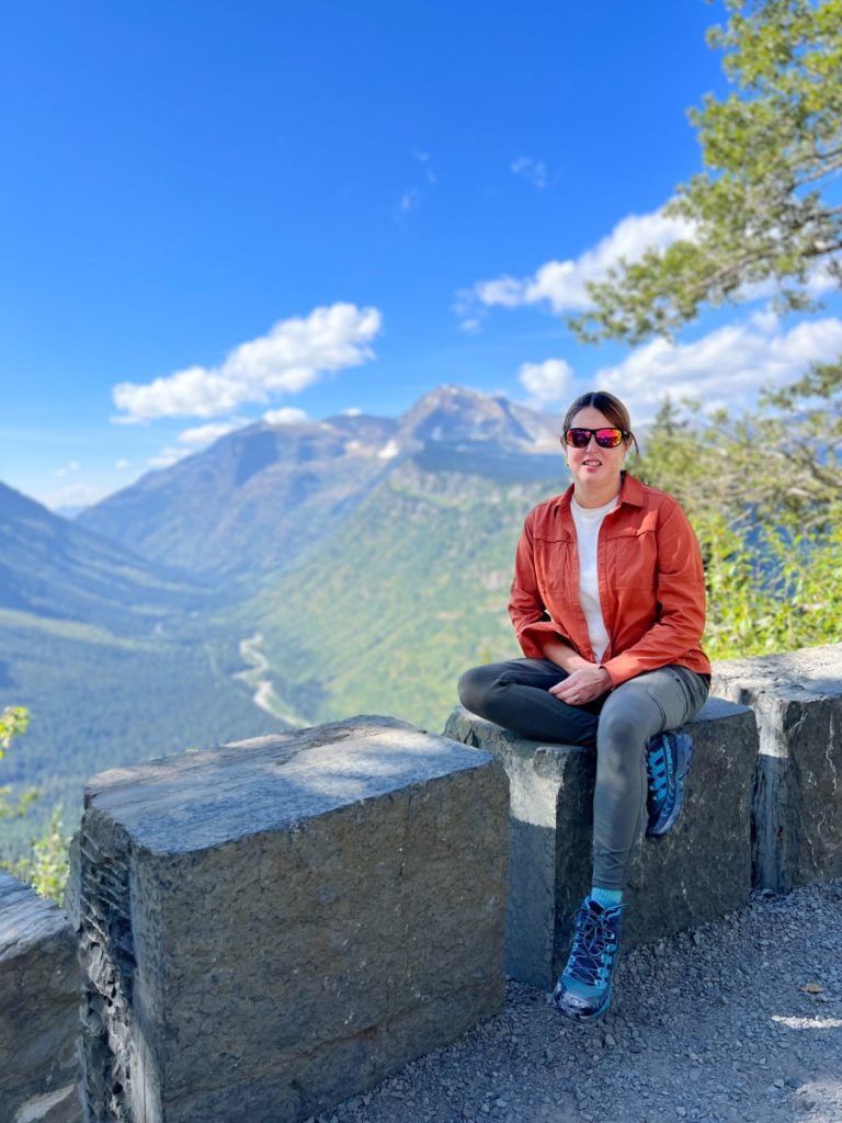 Tamara sitting on rock wall at overlook int Glacier National Park
