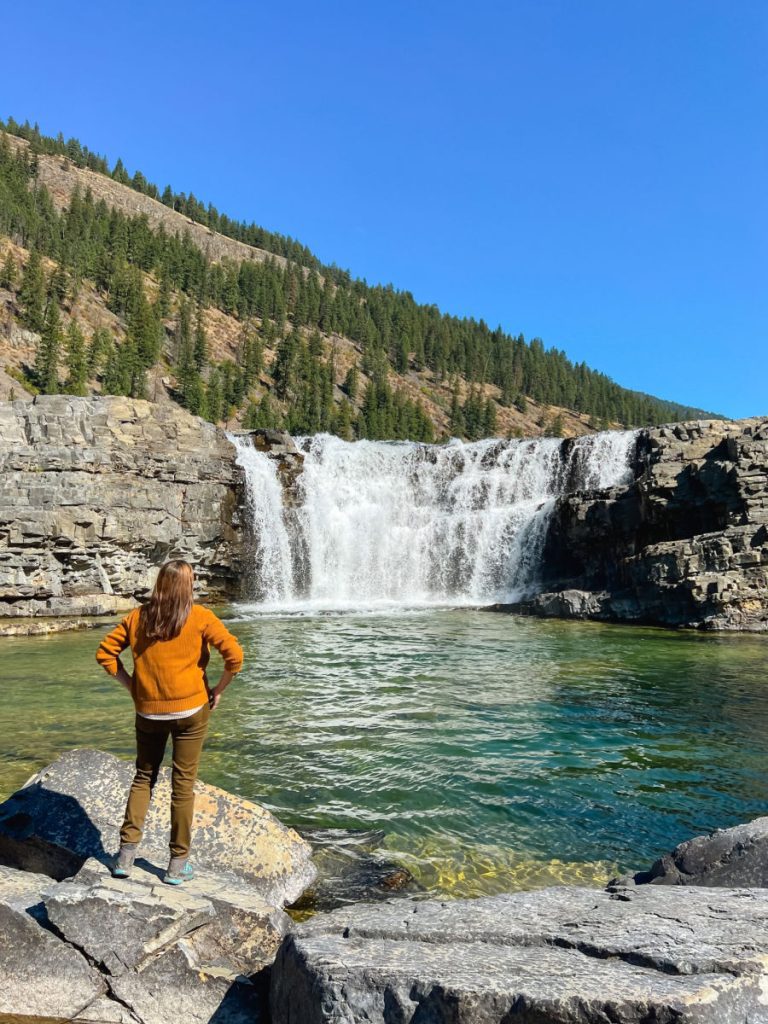 Tamara in orange sweater standing in front of Kootenai falls
