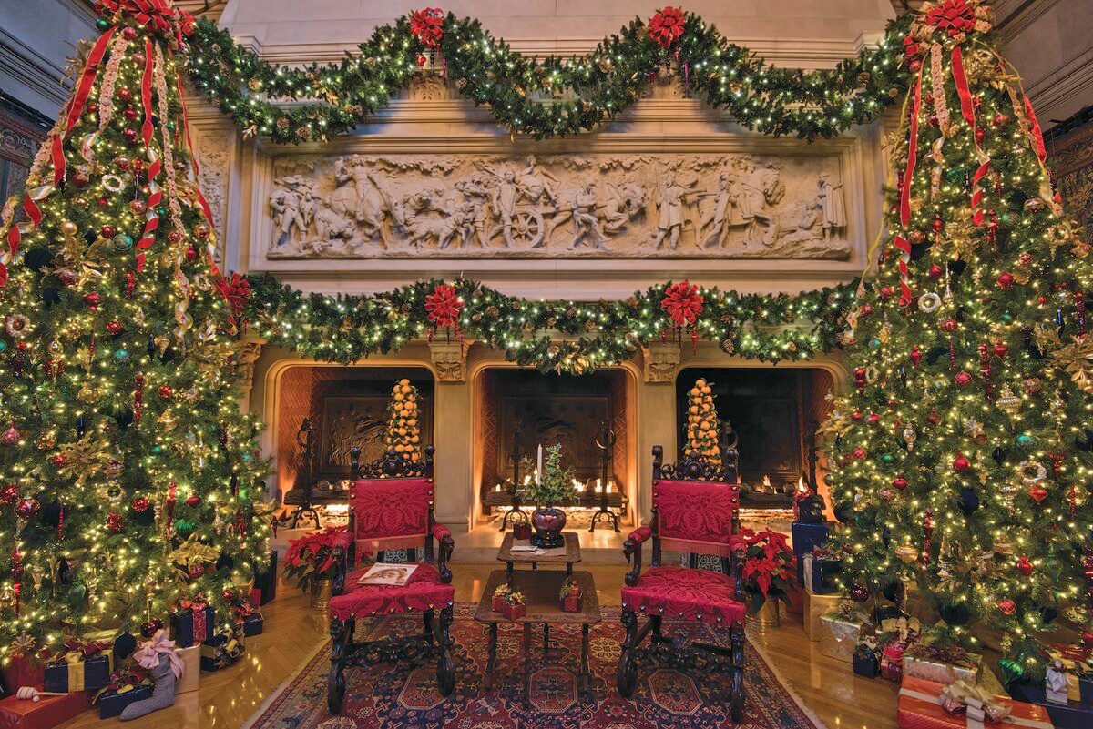 Banquet hall at Biltmore decorated for the holidays with two large christmas trees and two red chairs in front of a large fireplace