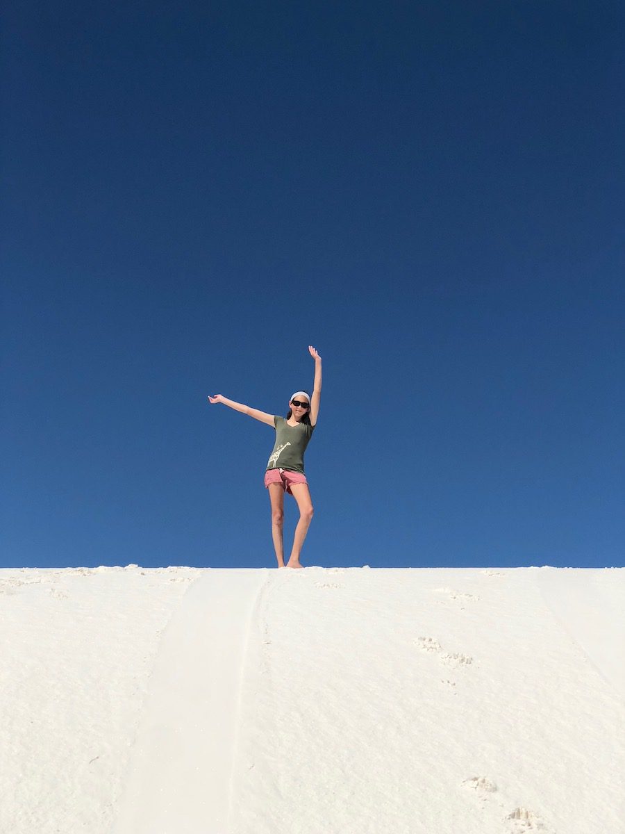 Hannah with arms up on top of white sand dune