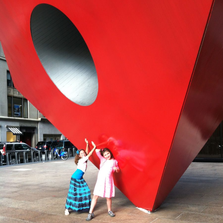 2 girls pushing on red sculpture