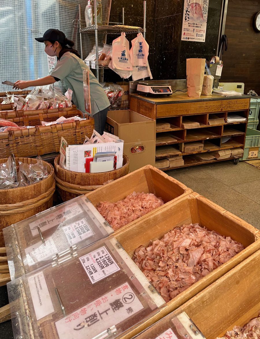 Fish market seller with bins of bonito flakes