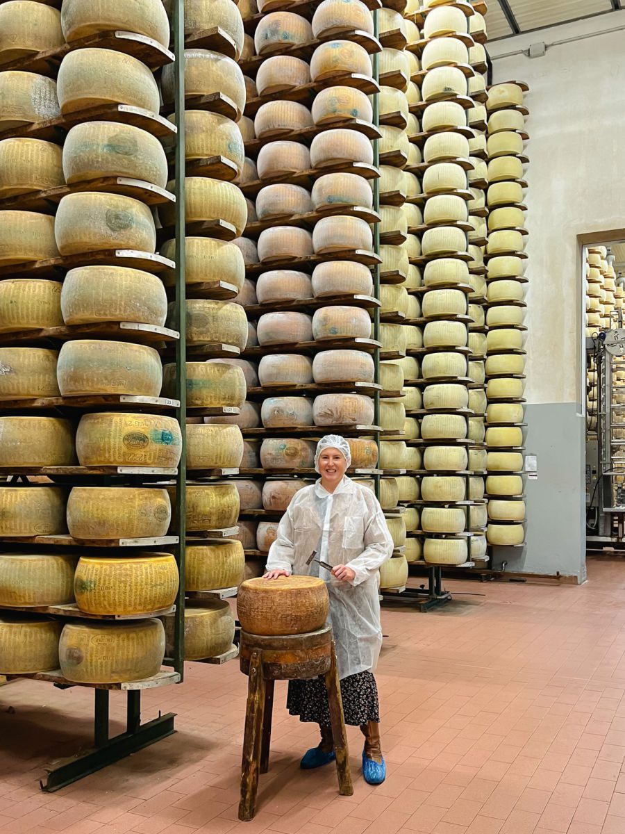 Tamara in Parmesan cheese factory with stack of cheese wheels