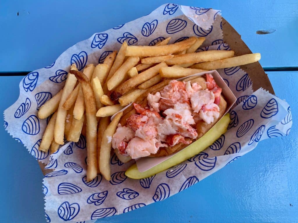 Maine lobster roll french fries and a pickle on a blue background