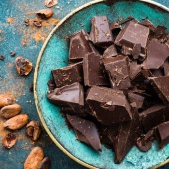 Broken pieces of chocolate on a plate surrounded by cacao beans