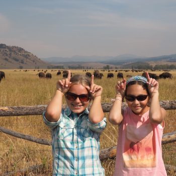 Two girls in front of bison making pretend horns on their heads