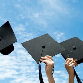 Graduation hats held in the air against a blue sky